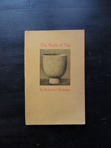 Book cover with a cup for tea in black and white with sepia toned background. The title of the book is The Book of Tea  by Kakuzo Okakura.